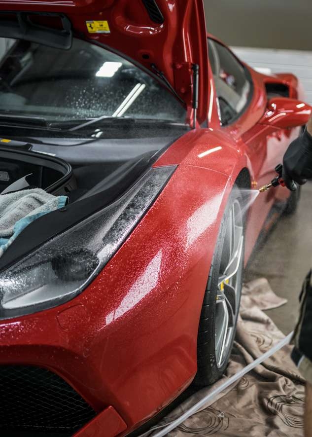 Red Ferrari 458 GTB car side being sprayed with water to prepare for paint protection film (PPF) application
