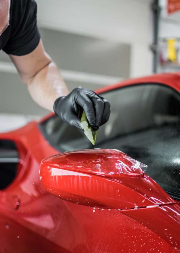 Paint protection film (PPF) being applied to side mirror of red Ferrari 458 GTB