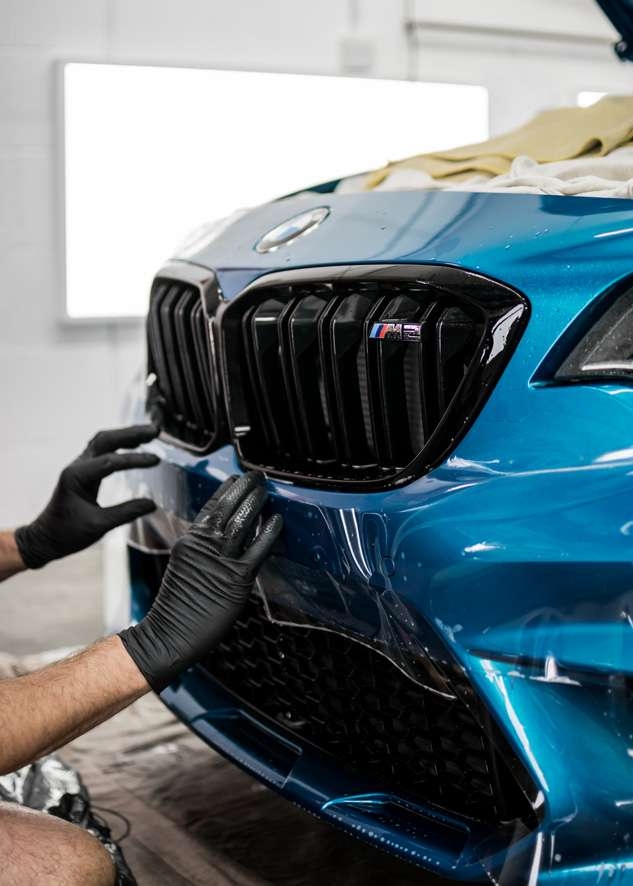 Paint protection film (PPF) being applied to front bumper of blue BMW M2C