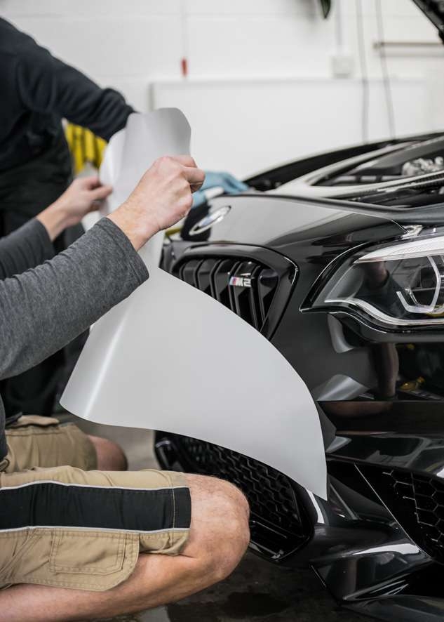 Paint protection film (PPF) being applied to front bumper of black BMW M2C