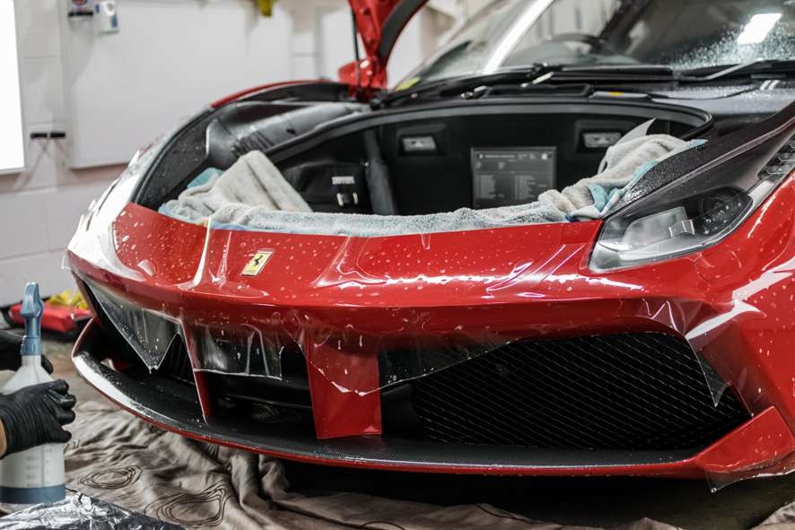 Paint protection film (PPF) being applied to front bumper of red Ferrari 458 GTB