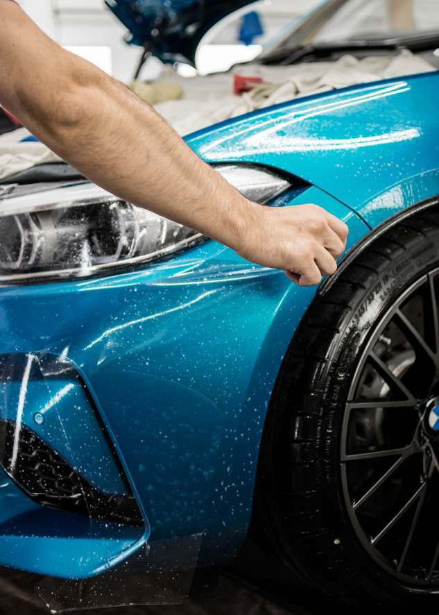Paint protection film (PPF) being applied to front bumper of blue BMW M2C