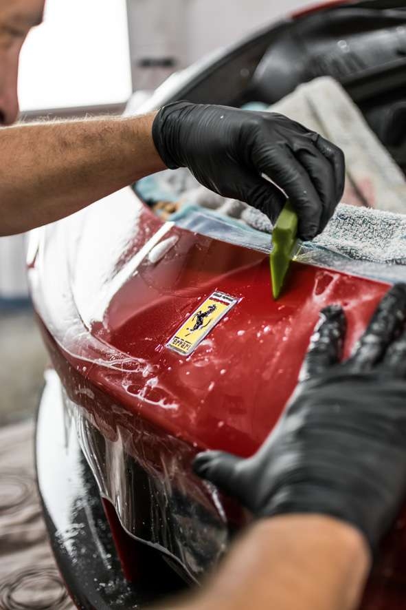 Paint protection film (PPF) being applied to red Ferrari 458 GTB badge and front bumper